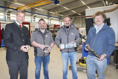 Olaf Heinrich, Max Scharringer, Michael Pauli und Helmut Knaus mit verschiedenen Teilen, die (v. l.) in der Hydraulik eines Baggers, einem Meilerkipper, der Fassade in Dubai oder dem Ölverteiler eines Baggers gebraucht werden.