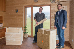 Christian Eiler (l.) präsentierte Bezirkstagspräsident Dr. Olaf Heinrich (r.) das Modell eines Wandaufbaus aus Holz samt Hobelspan-Lehm-Dämmung sowie innen Stroh- und außen Heraklitplatten. 