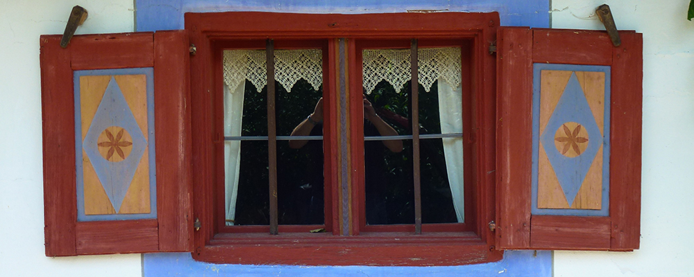 In Blau- und Brauntönen gehaltenes Fenster mit Läden eines denkmalgeschützten bäuerlichen Anwesens